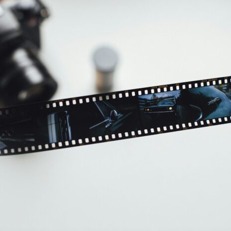 Photo by Markus Spiske Close-up of a hand holding a vintage film strip with a blurred camera in the background, evoking nostalgia.