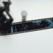 Close-up of a hand holding a vintage film strip with a blurred camera in the background, evoking nostalgia.