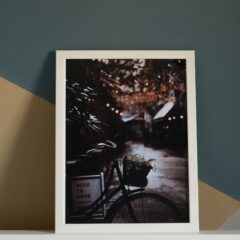 Framed photo of a bicycle in an urban setting with ambient lighting, displayed on a stylish wall.